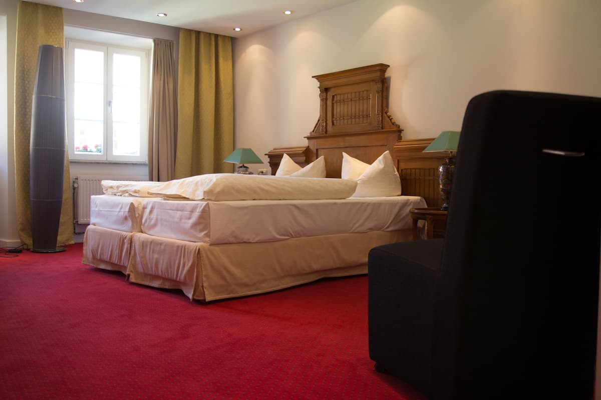 A hotel room with a large bed, a wooden headboard, a red carpet, and a window with curtains.