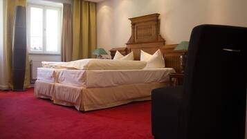 A hotel room with a large bed, a wooden headboard, a red carpet, and a window with curtains.