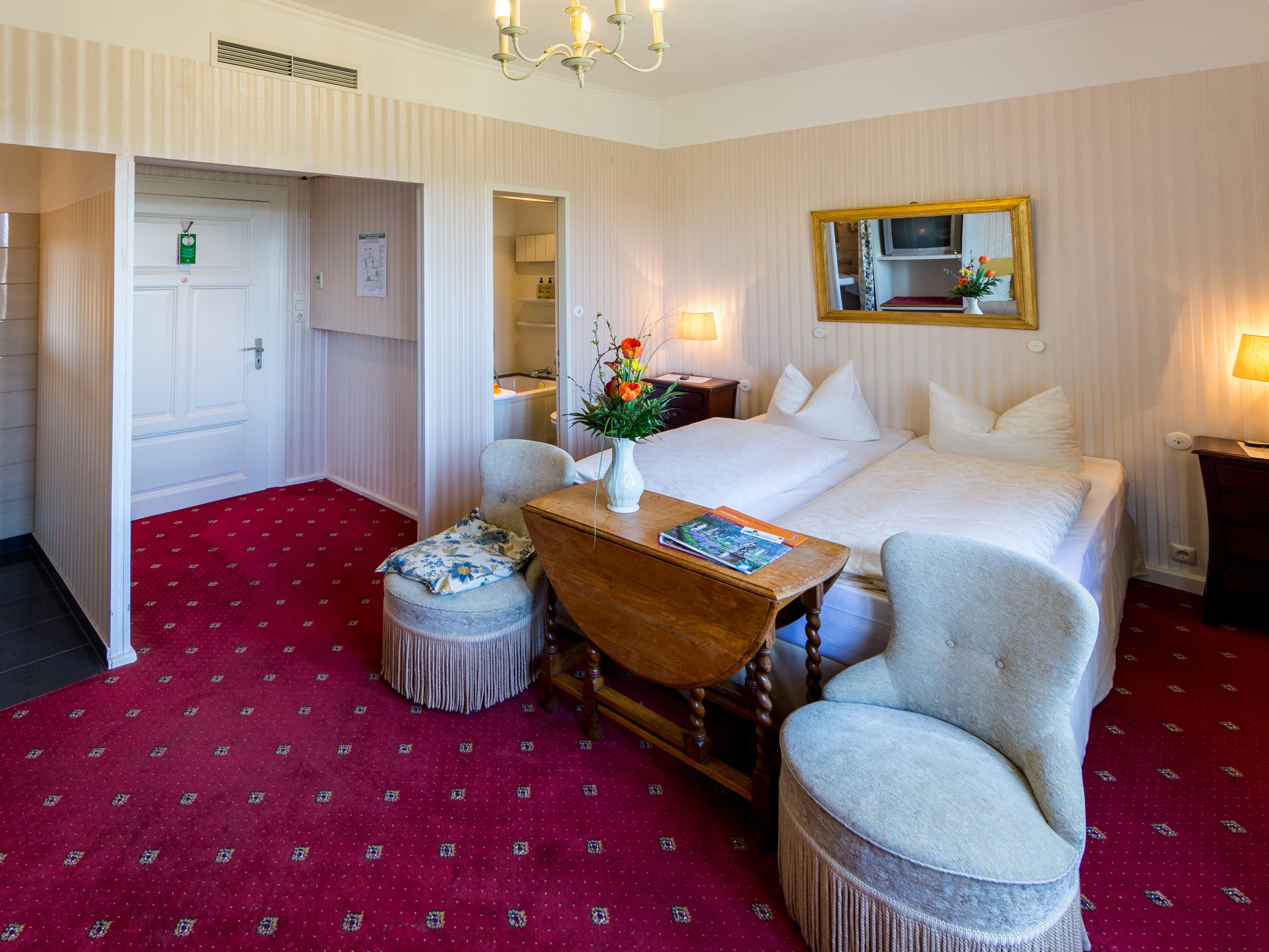 Une chambre d’hôtel avec un grand lit, une table de chevet en bois, une chaise, une petite table et un miroir au mur.