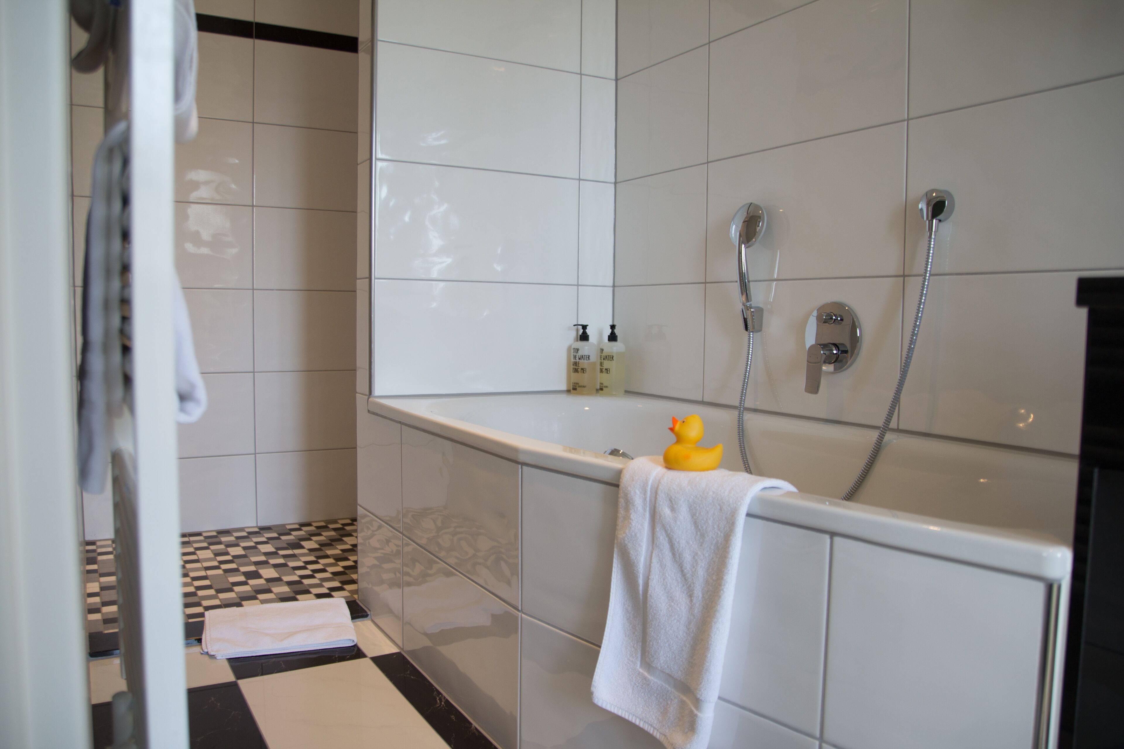 Un baño con una bañera, dos cabezales de ducha, un patito de goma y un perchero para toallas.