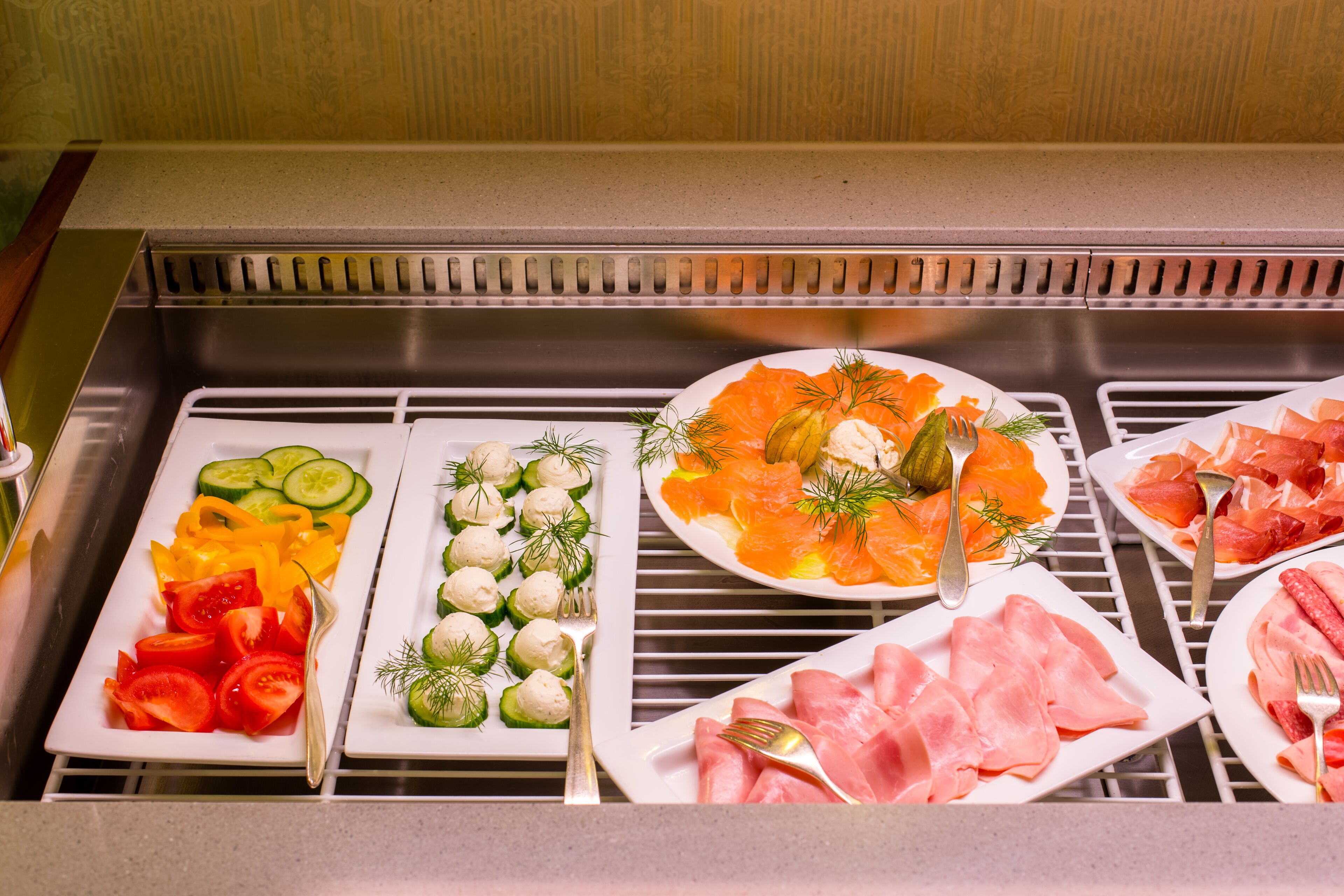Ein Buffet mit verschiedenen Speisen, darunter Tomatenscheiben, Gurken, eingelegtes Gemüse, Räucherlachs und Aufschnitt.
