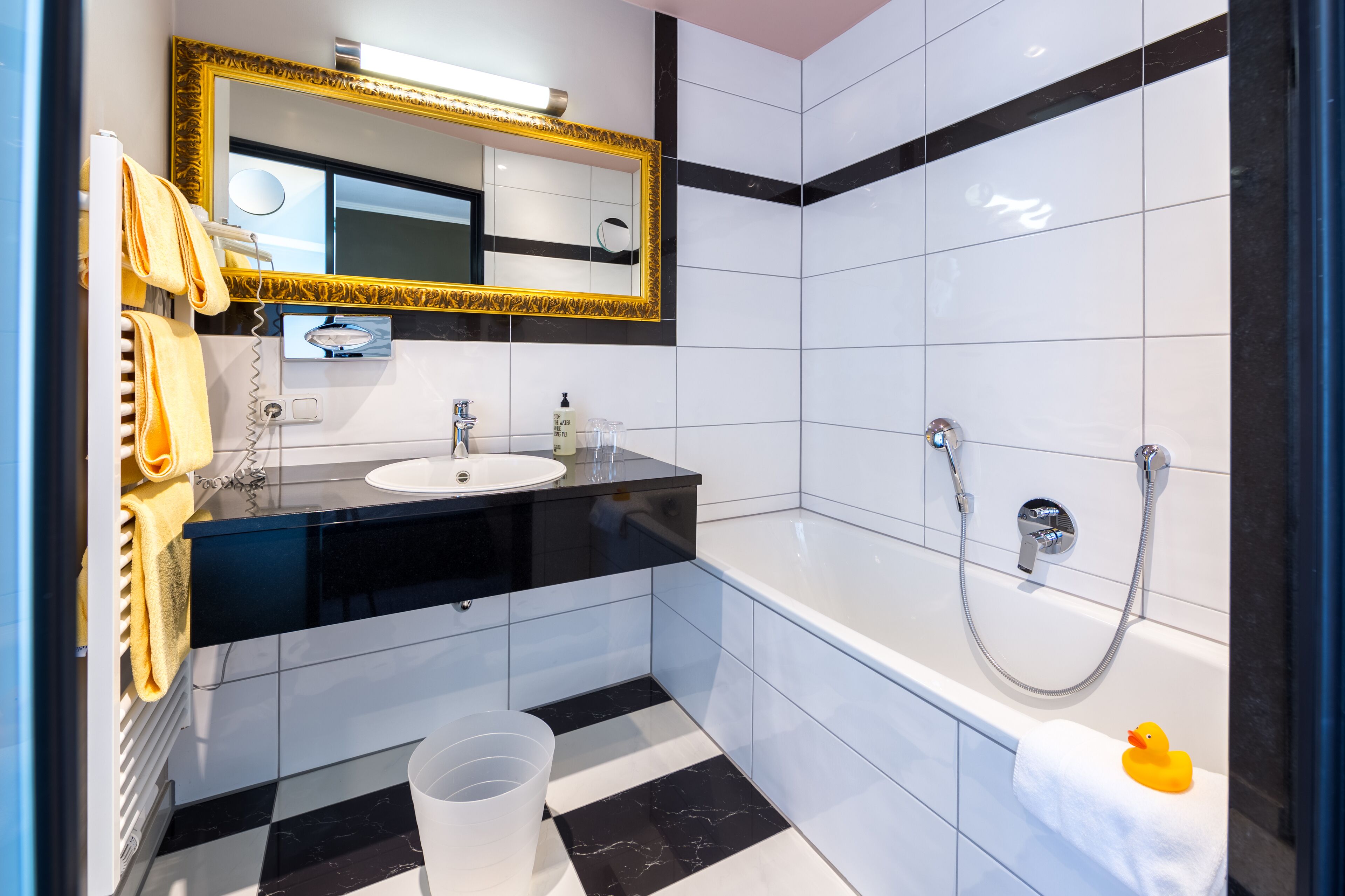 Ein modernes Badezimmer mit einem schwarzen Waschtisch, einem Spiegel mit goldener Rahmung, einer weißen Badewanne und einer Dusche.