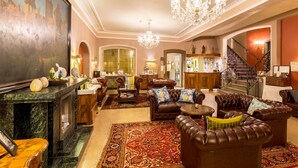 A spacious lobby with a grand staircase, leather sofas, a marble fireplace, and a large painting. - Hotel Goldener Hirsch (Rothenburg ob der Tauber)