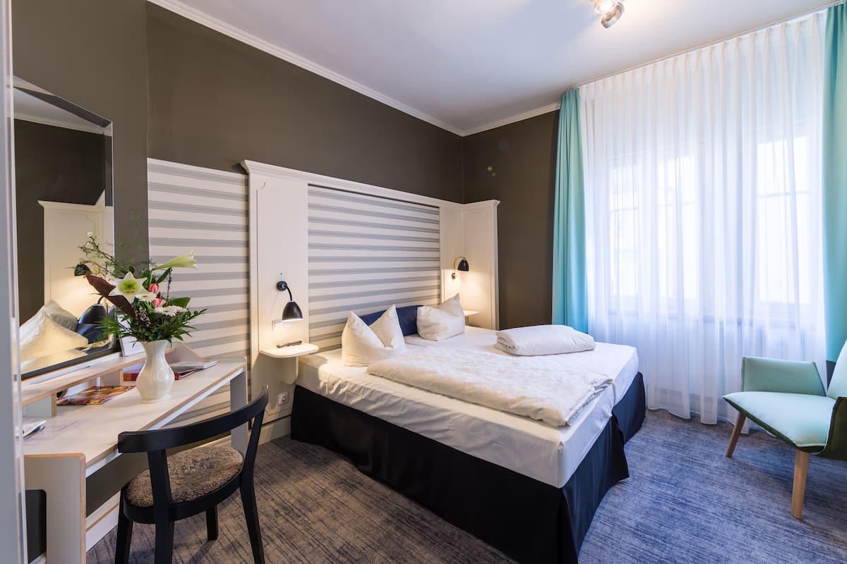 A hotel room with a bed, desk, chair, and a large mirror.