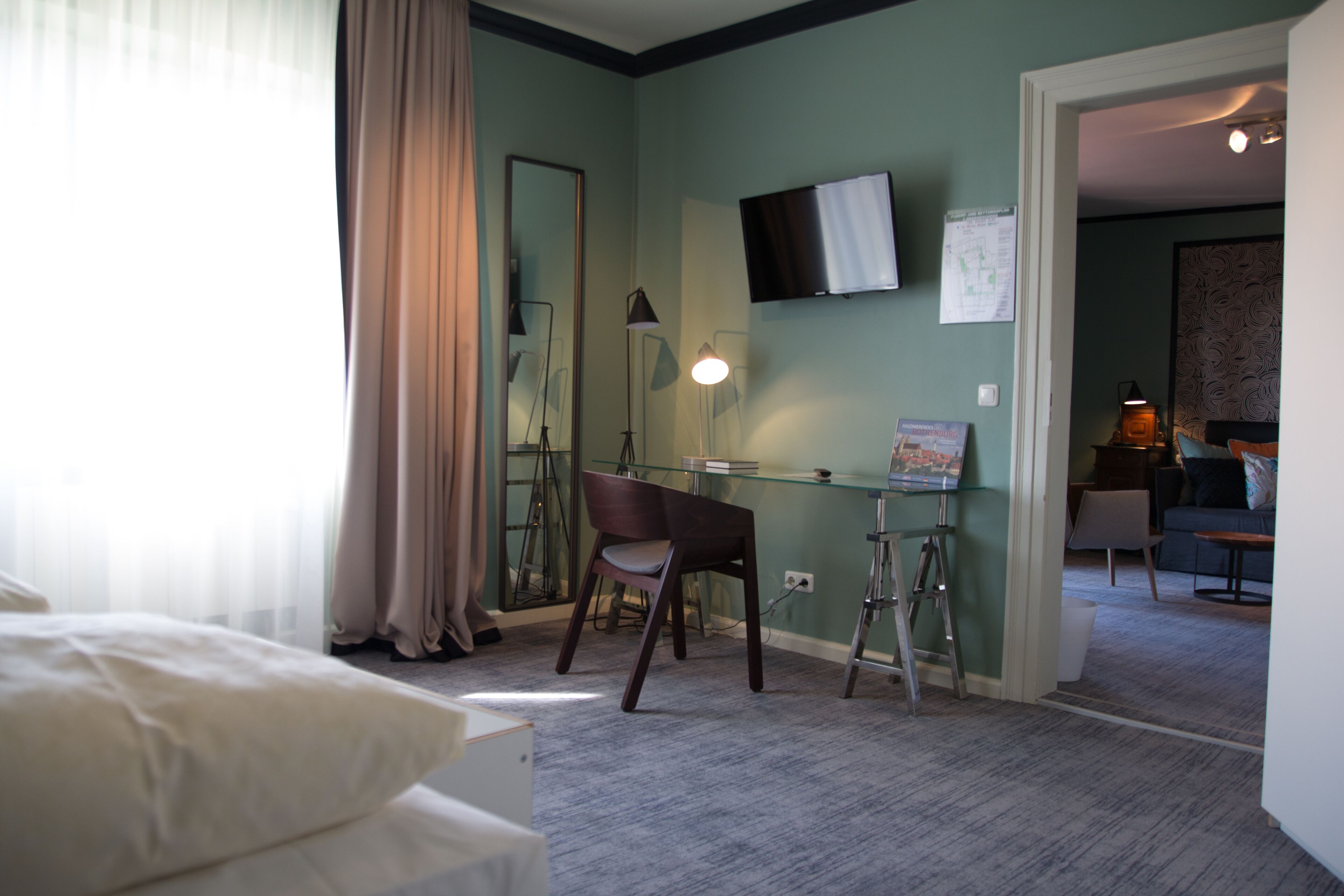 Habitación de hotel con cama, escritorio con silla, televisión montada en la pared y lámpara.