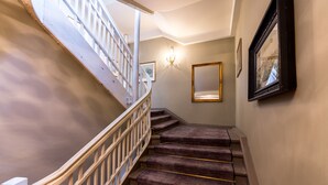 A staircase with a white railing, carpeted steps, and a chandelier. - Hotel Goldener Hirsch (Rothenburg ob der Tauber)