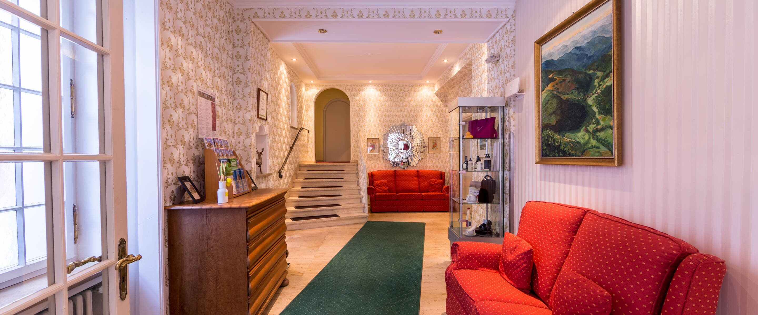 A hallway with a red sofa, a wooden dresser, a green rug, and a painting on the wall.