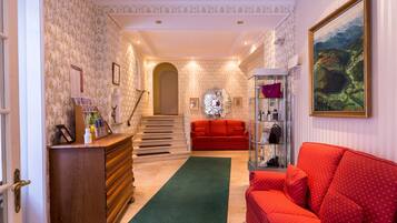 A hallway with a red sofa, a wooden dresser, a green rug, and a painting on the wall.