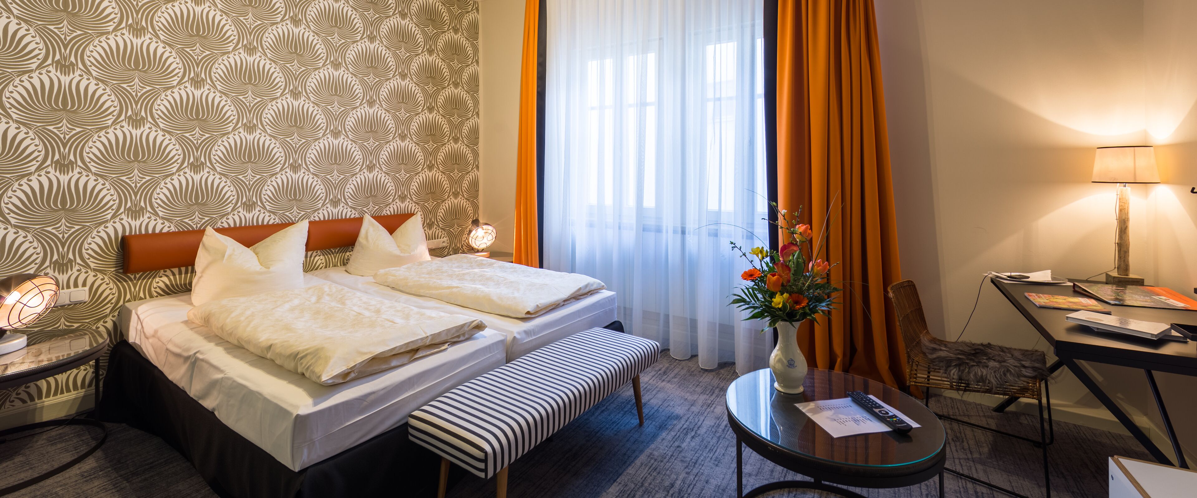 Ein Hotelzimmer mit Bett, Nachttischen, Schreibtisch, Stuhl und einem fenster mit Vorhängen.