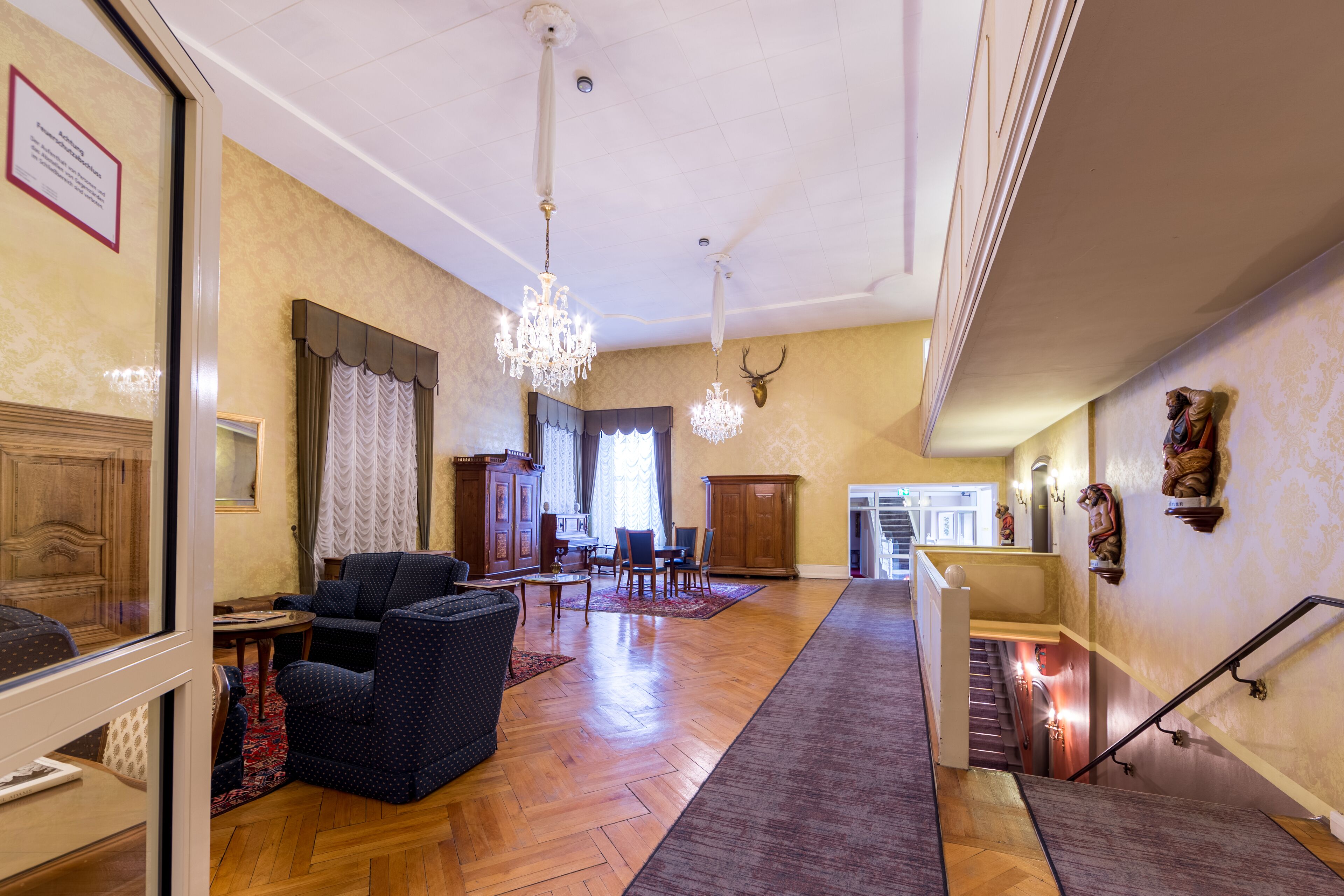 A spacious lobby with a wooden floor, a chandelier, and a staircase.