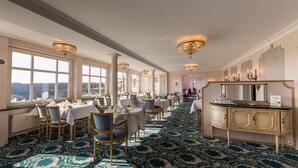 A long dining hall with tables and chairs, chandeliers, and a view through large windows. - Hotel Goldener Hirsch (Rothenburg ob der Tauber)