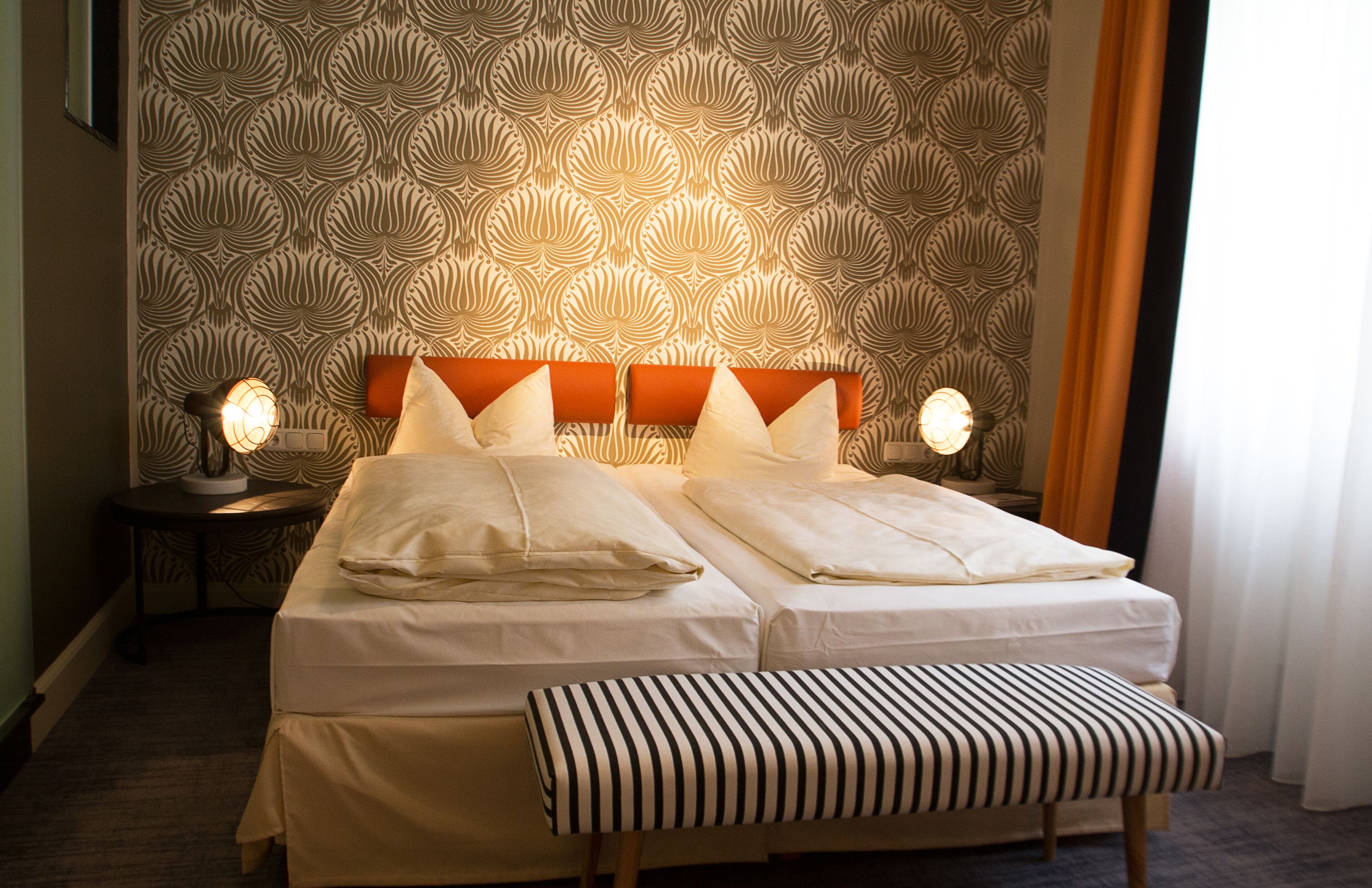 Ein Doppelbett mit gestreifter Sitzbank, zwei Nachttischen und strukturierter Tapete.