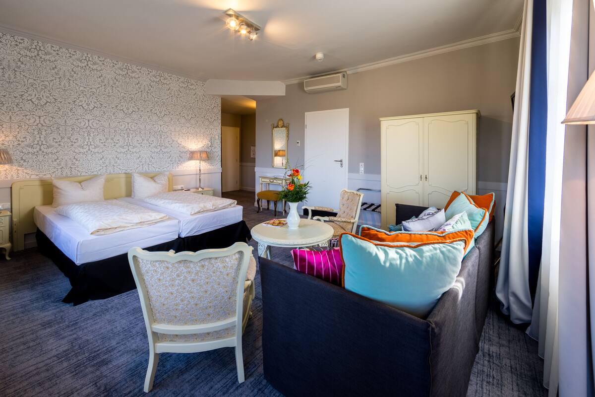 A hotel room with two beds, a sofa, a chair, a small table, and a mirror.