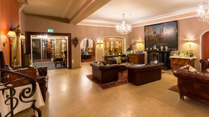 A spacious lobby with leather sofas, a grand chandelier, and a large painting on the wall. - Hotel Goldener Hirsch (Rothenburg ob der Tauber)