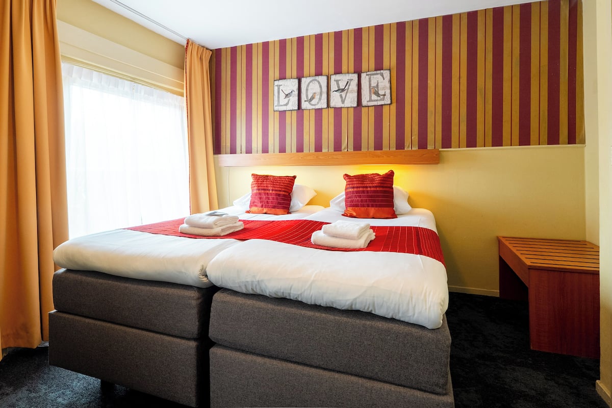 A hotel room with a bed, two pillows, a bedside table, and a wall with the word "LOVE" spelled out.
