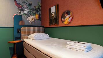 A hotel room with a bed, a nightstand, a wall-mounted lamp, a painting, and a mirror.