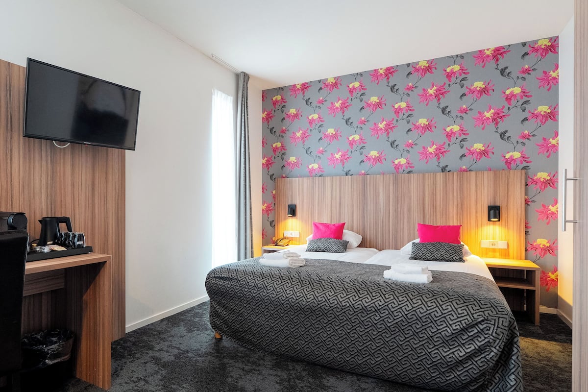 A hotel room with a large bed, two bedside tables with lamps, a flat-screen TV mounted on the wall, and a desk with a coffee maker and cups.