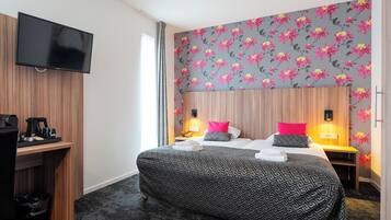 A hotel room with a large bed, two bedside tables with lamps, a flat-screen TV mounted on the wall, and a desk with a coffee maker and cups.