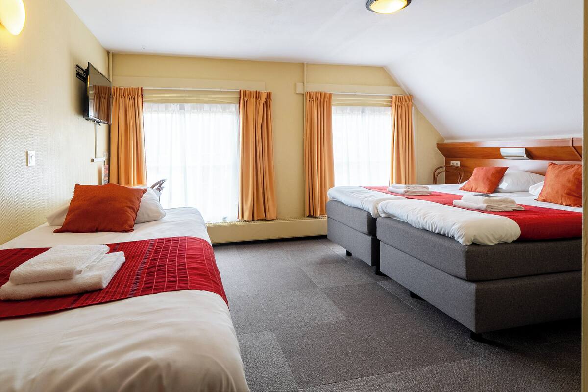 A hotel room with two beds, a flat-screen TV, a ceiling light, and a window with curtains.