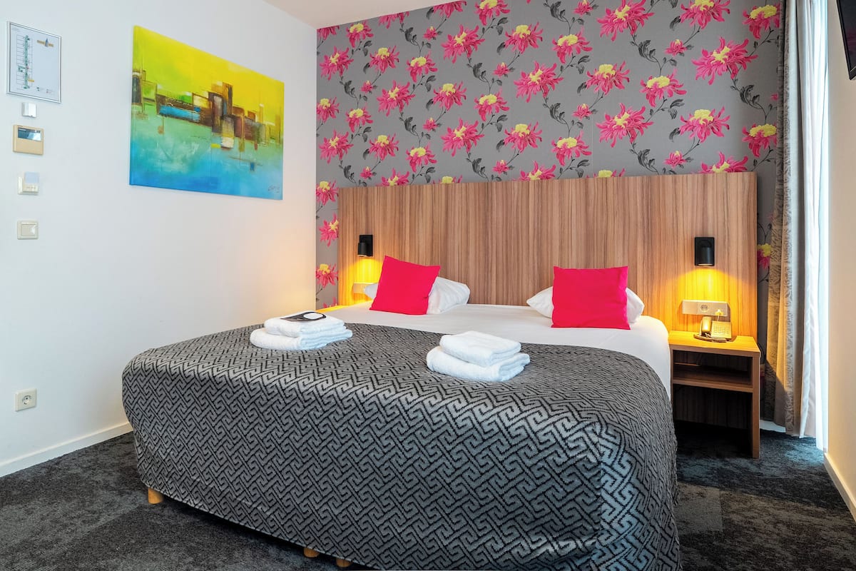 A hotel room with a large bed, two bedside tables with lamps, a floral wallpaper, and a painting on the wall.