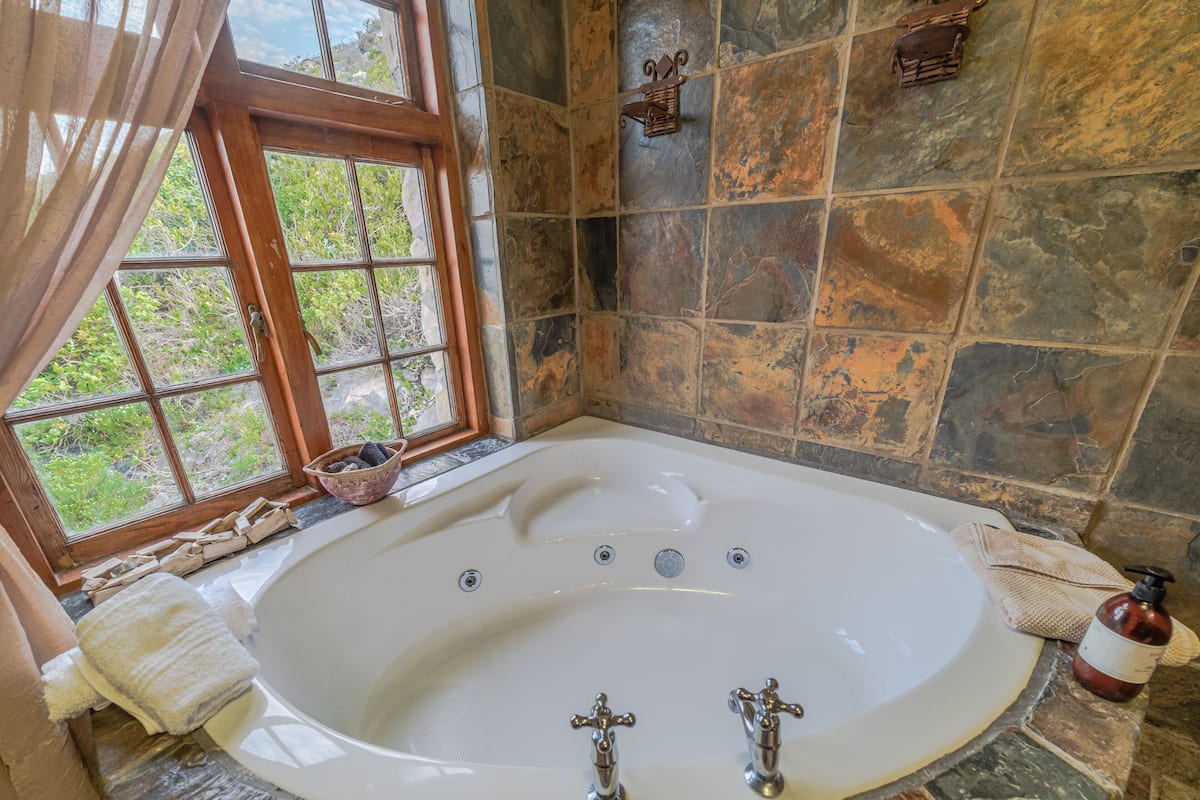 A bathroom with a large bathtub, a window, and stone walls.