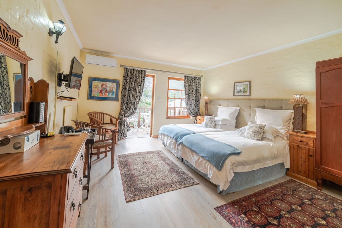 A bedroom with a bed, bedside tables, a desk, and a chair. There is a window with curtains, a door, and a wall-mounted lamp.