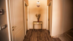 A hallway with a wooden floor, a small table with a vase, and a light fixture on the ceiling. - Il Monte (Monte San Savino)
