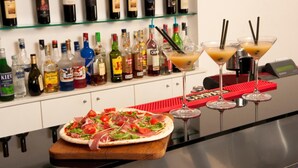 A bar area with a variety of liquor bottles, a pizza on a wooden board, and three martini glasses with straws. - Il Monte (Monte San Savino)