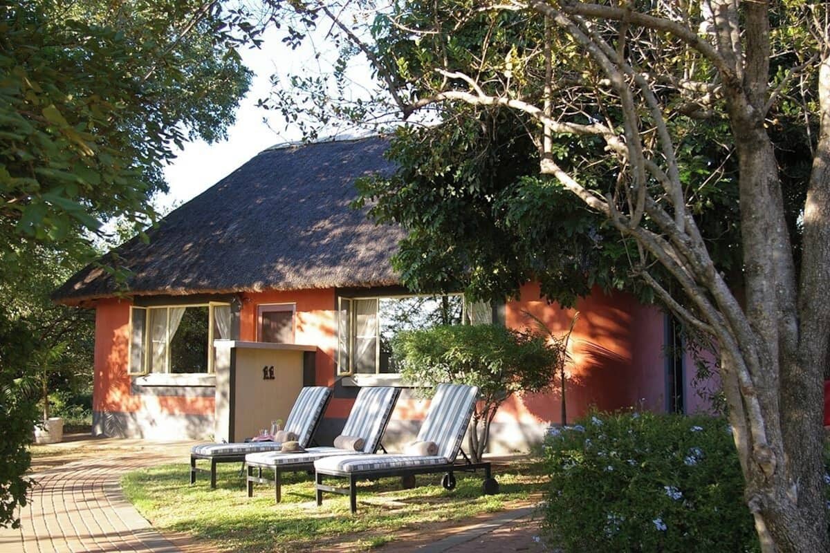 A bungalow with a thatched roof, two lounge chairs, and a small table.
