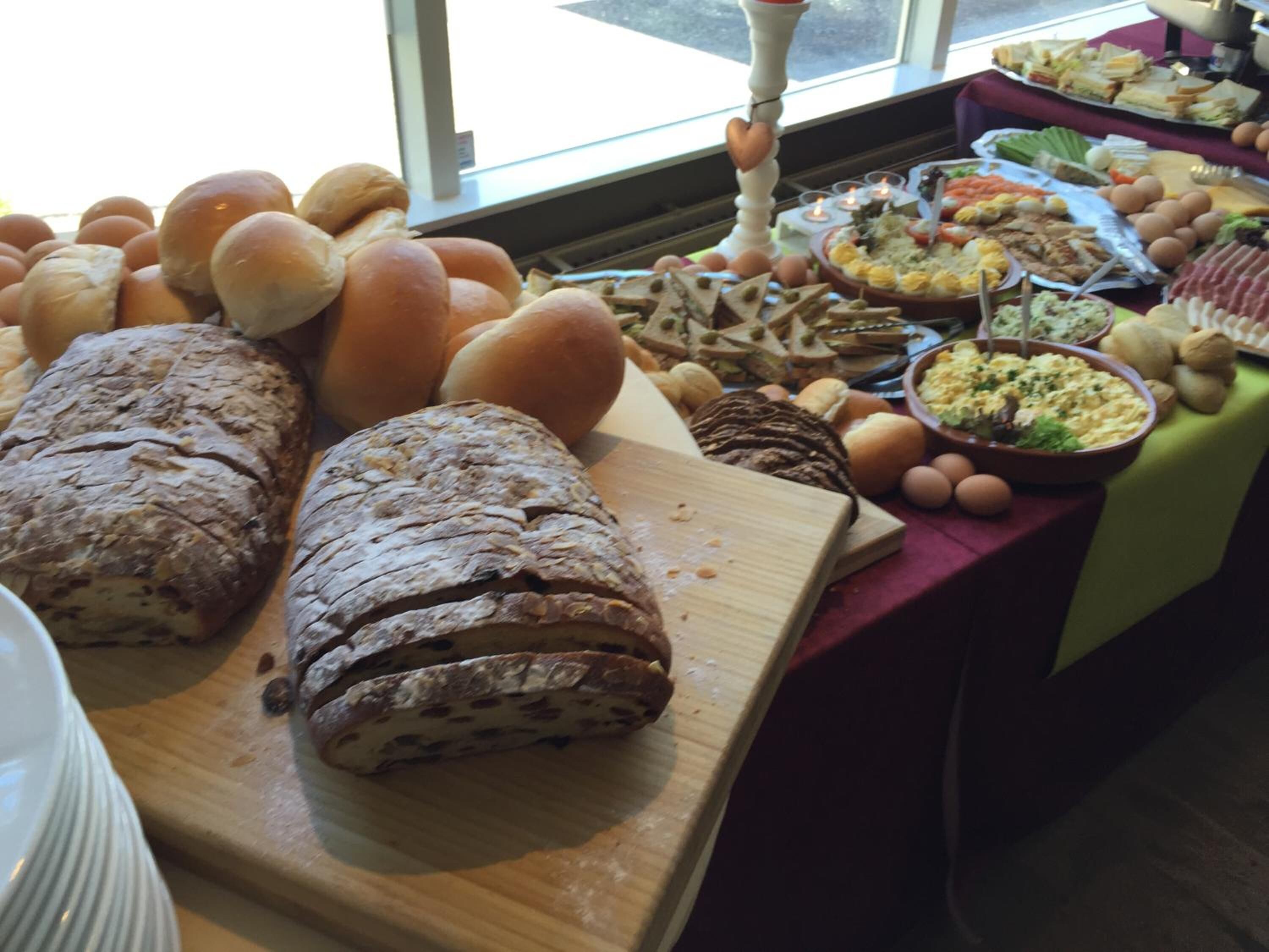 A buffet table with various breads, sandwiches, and a variety of dishes including salads and eggs.