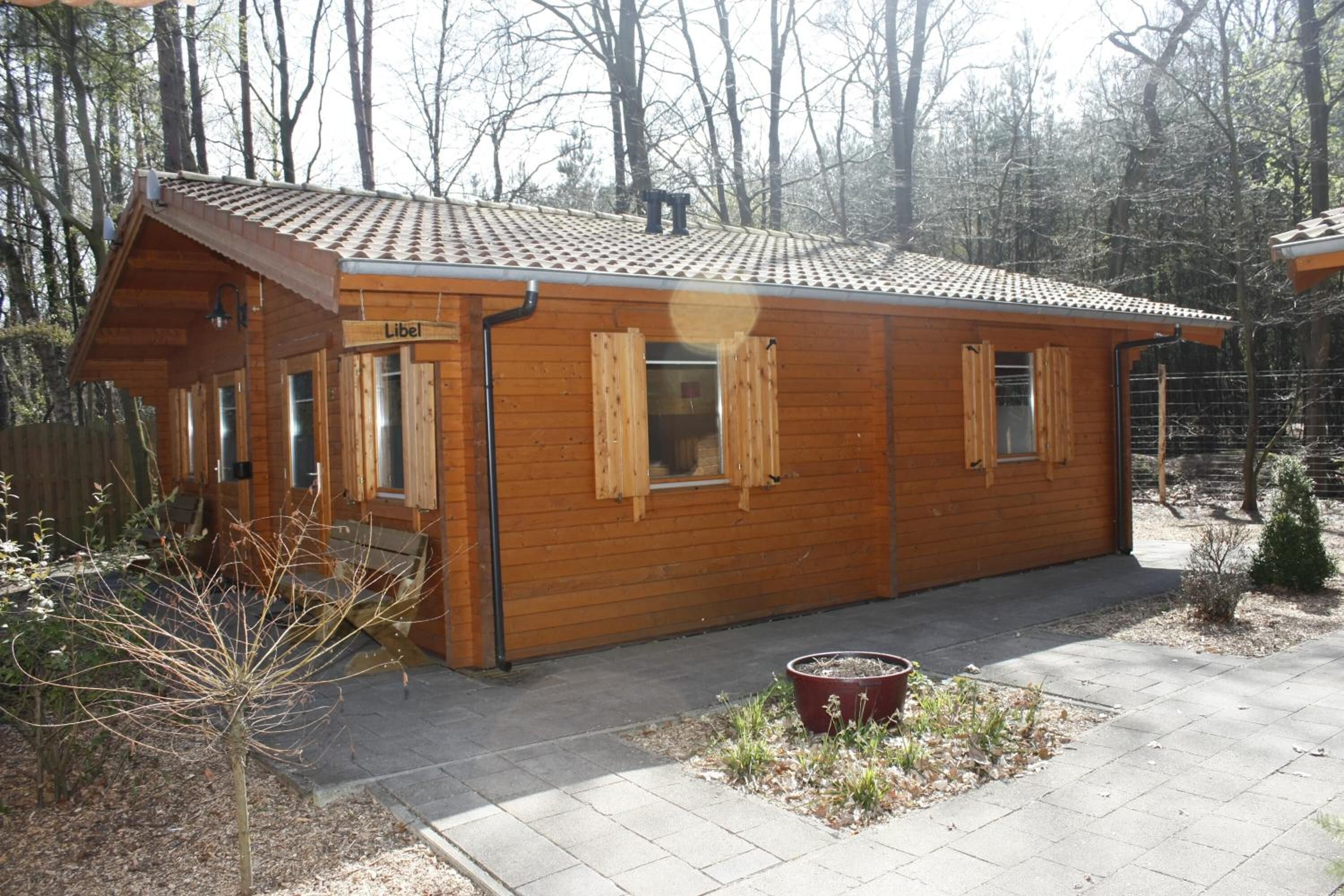 A wooden cabin with a tiled roof, a small porch, and a potted plant in front.