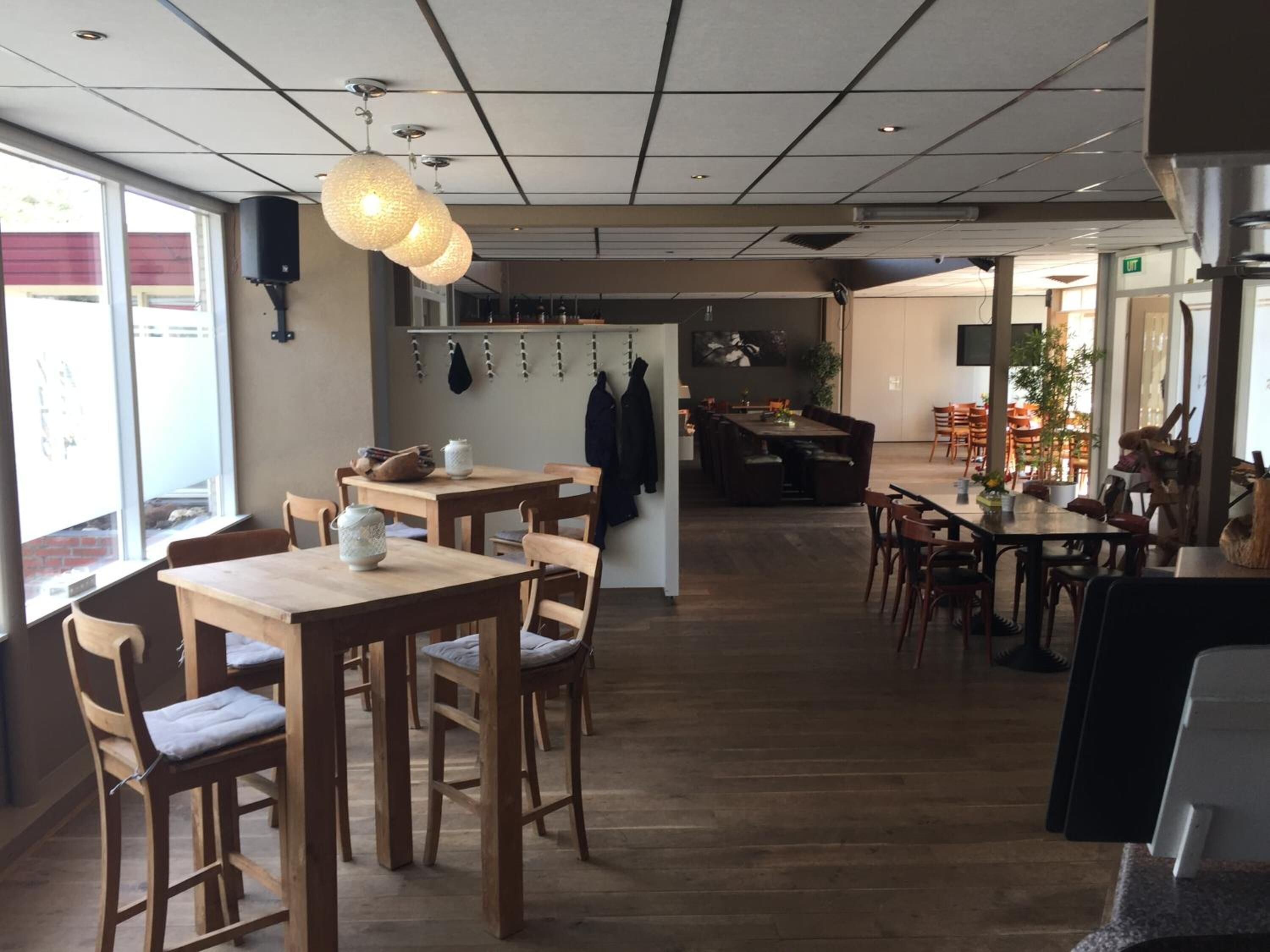 En restaurang med bord och stolar i trä, en hängande lampa och utsikt över omgivningen.
