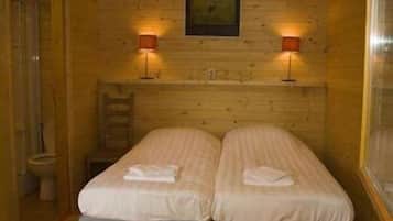 A small, cozy room with two single beds, a wooden wall, and two wall-mounted lamps.