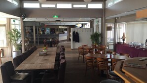 A spacious dining area with a long wooden table and multiple chairs, a bar area with stools, and a kitchen in the background. -  Lodges Veluwse Poort (Dieren)
