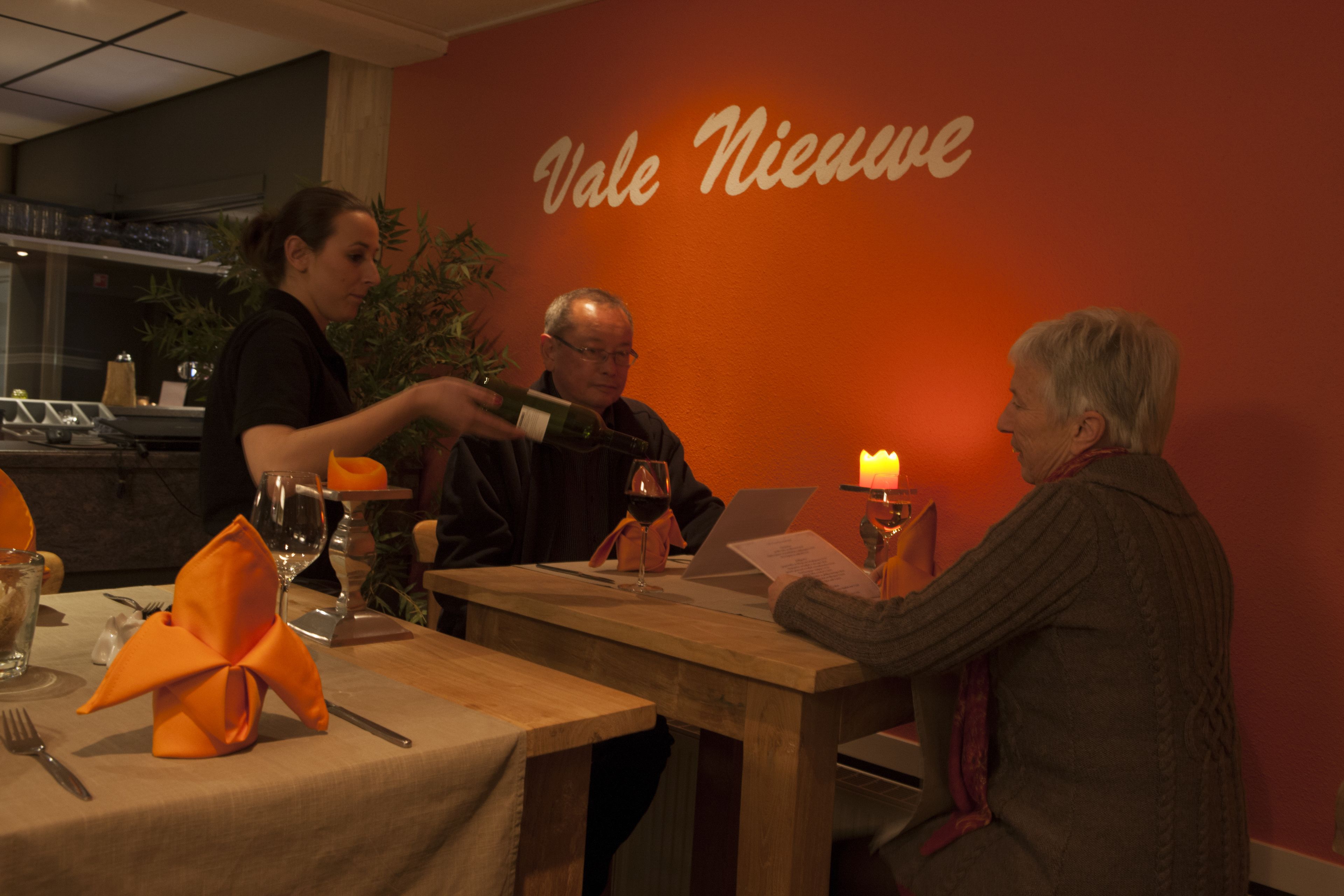 A restaurant interior with a wooden table set for a meal, a candle on the table, and a sign on the wall that reads "Vale Nieuve".