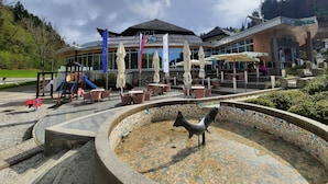 Un hotel con terraza, zona de juegos para niños y una fuente de mosaicos.