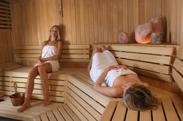Two wooden benches in a sauna with a copper bucket and stones on the wall.