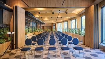 A conference room with rows of chairs, wooden walls, large windows, and a hexagonal patterned floor.