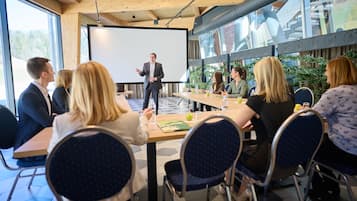 A conference room with a presentation screen, wooden ceiling, large windows, and a table with chairs.