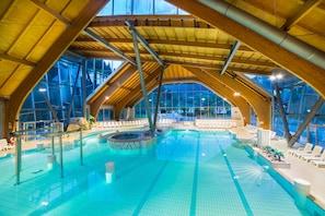 An indoor swimming pool with a high wooden ceiling and large windows. - Apartment Resort Eco Spa Snovik (Kamnik)