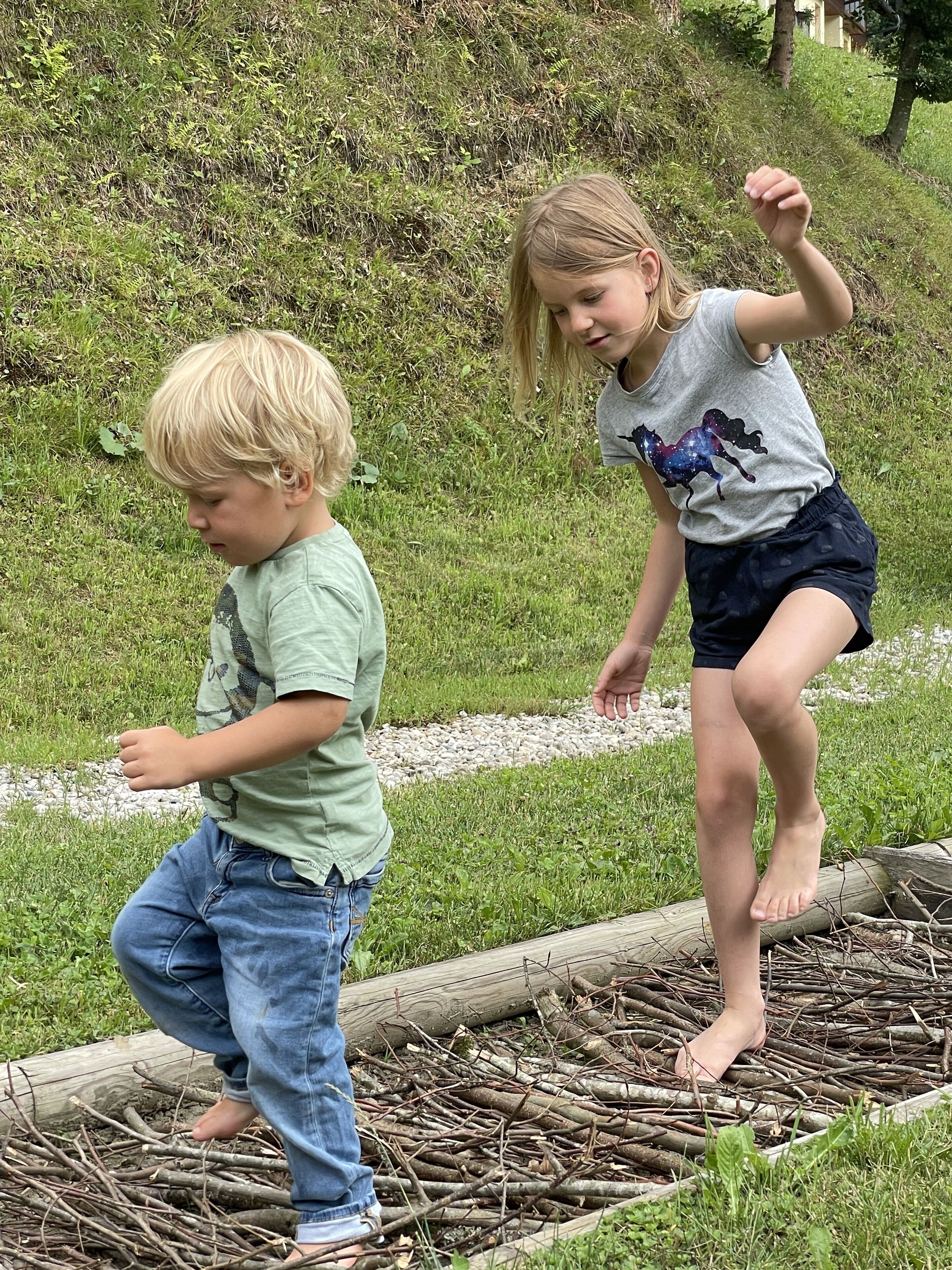 Twee kinderen spelen op een houten brug in een grasveld.