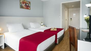 A hotel room with two beds, a nightstand, a desk, and a chair.