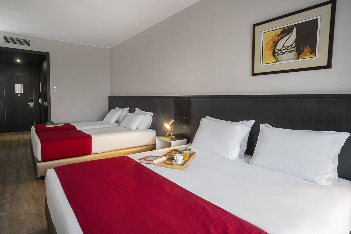 A hotel room with two beds, a red and white bedspread, a tray with a cup and a book, and a framed picture on the wall.