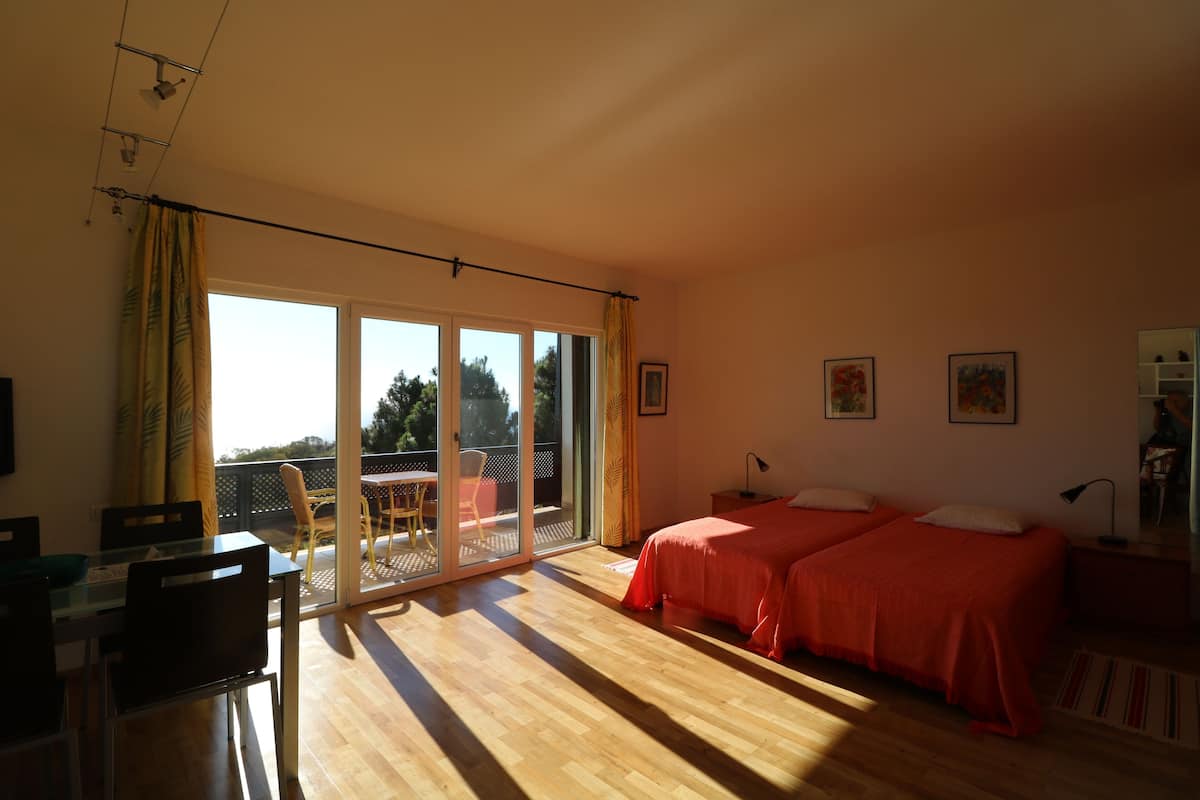 Un dormitorio con dos camas, una puerta corrediza de vidrio a un balcón, un comedor y una mesita.