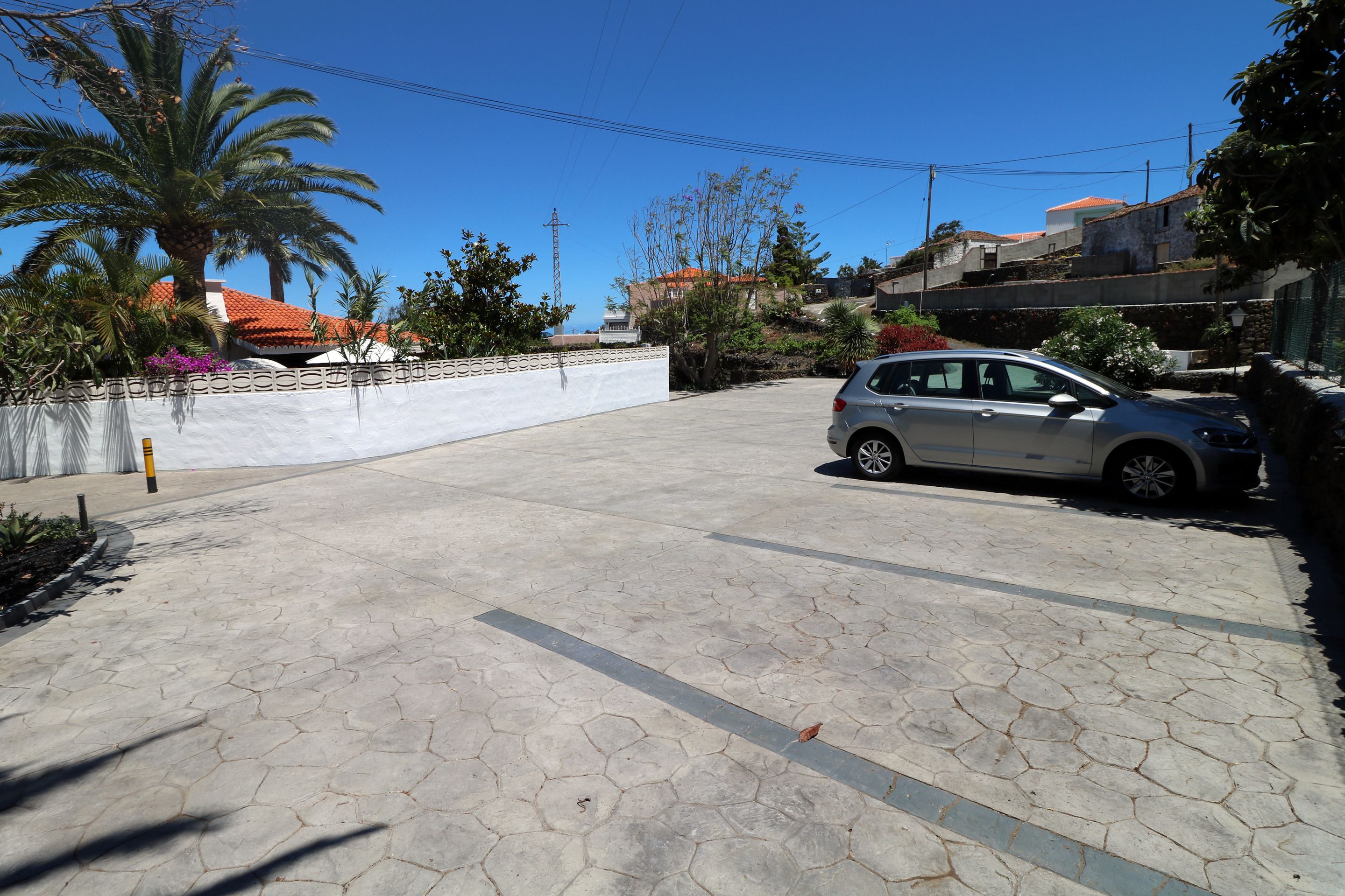 Un’area di parcheggio pavimentata con un'auto, palme e un muro bianco con decorazioni.
