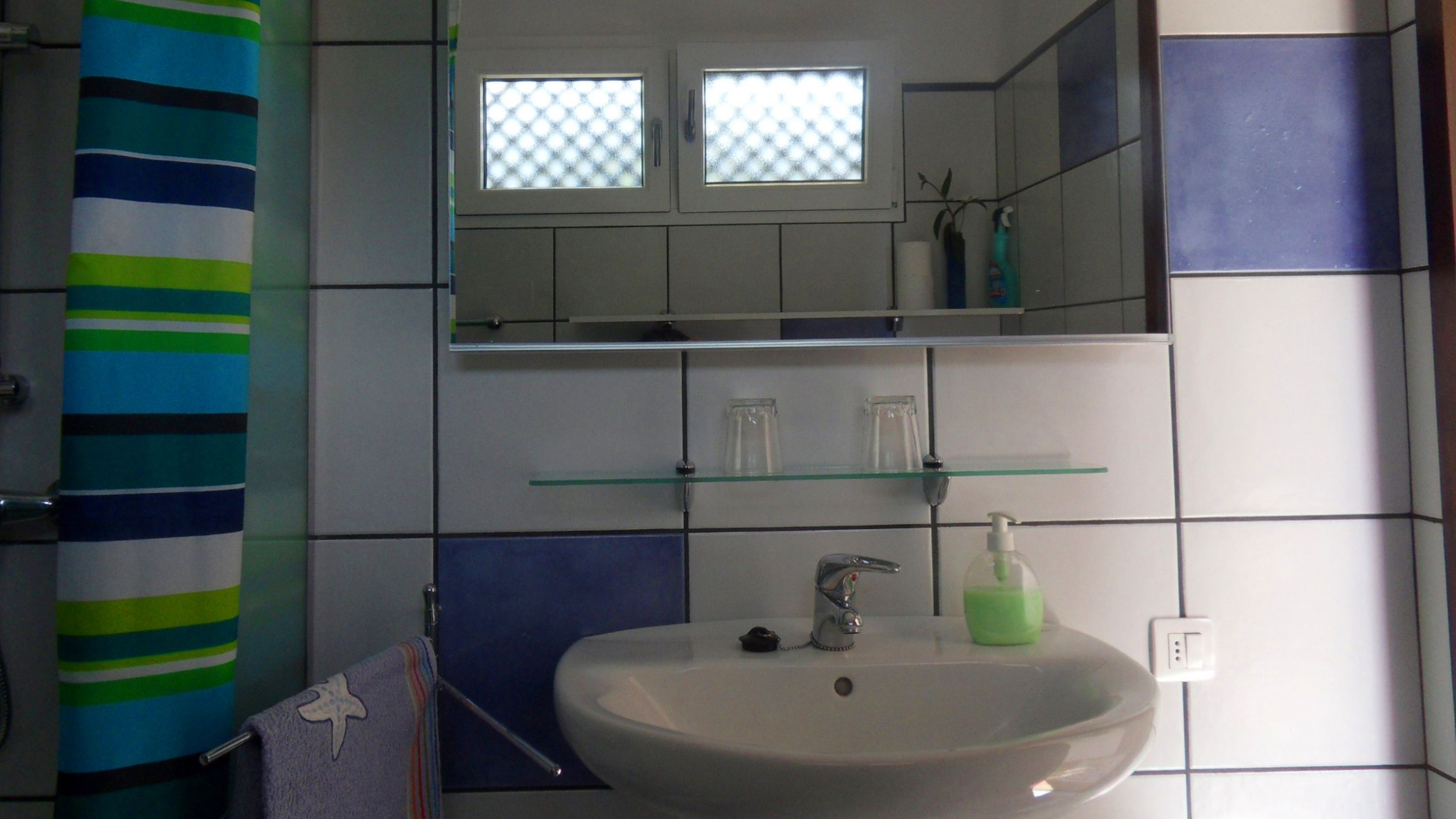 A bathroom with a white sink, a glass shelf above it, and a striped shower curtain.