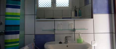 A bathroom with a white sink, a glass shelf above it, and a striped shower curtain.