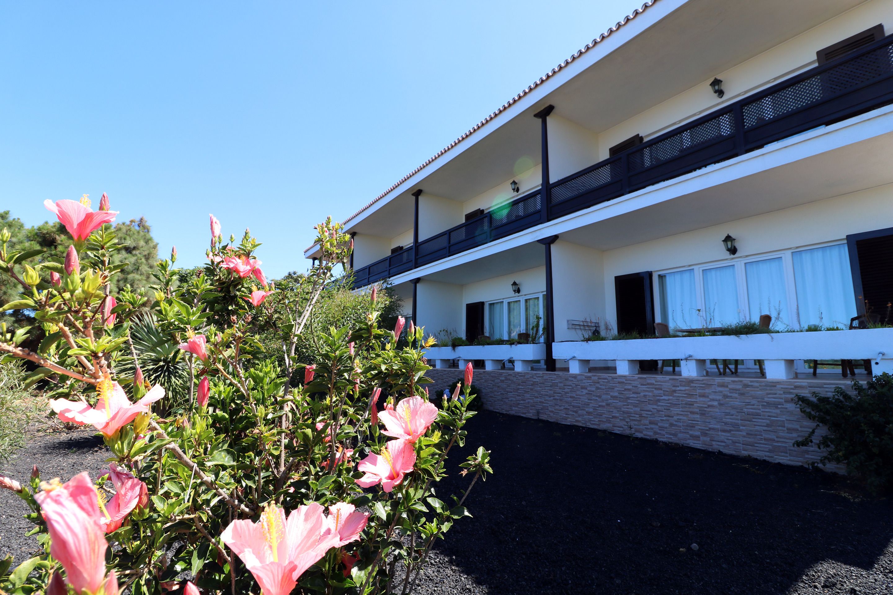 Ein zweistöckiges Gebäude mit Balkon, Backsteinmauer und Garten mit rosa Blüten.
