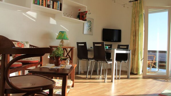 A living room with a wooden table, chairs, a TV, and a balcony with a yellow curtain. - Apartamentos Miranda (Brena Alta)
