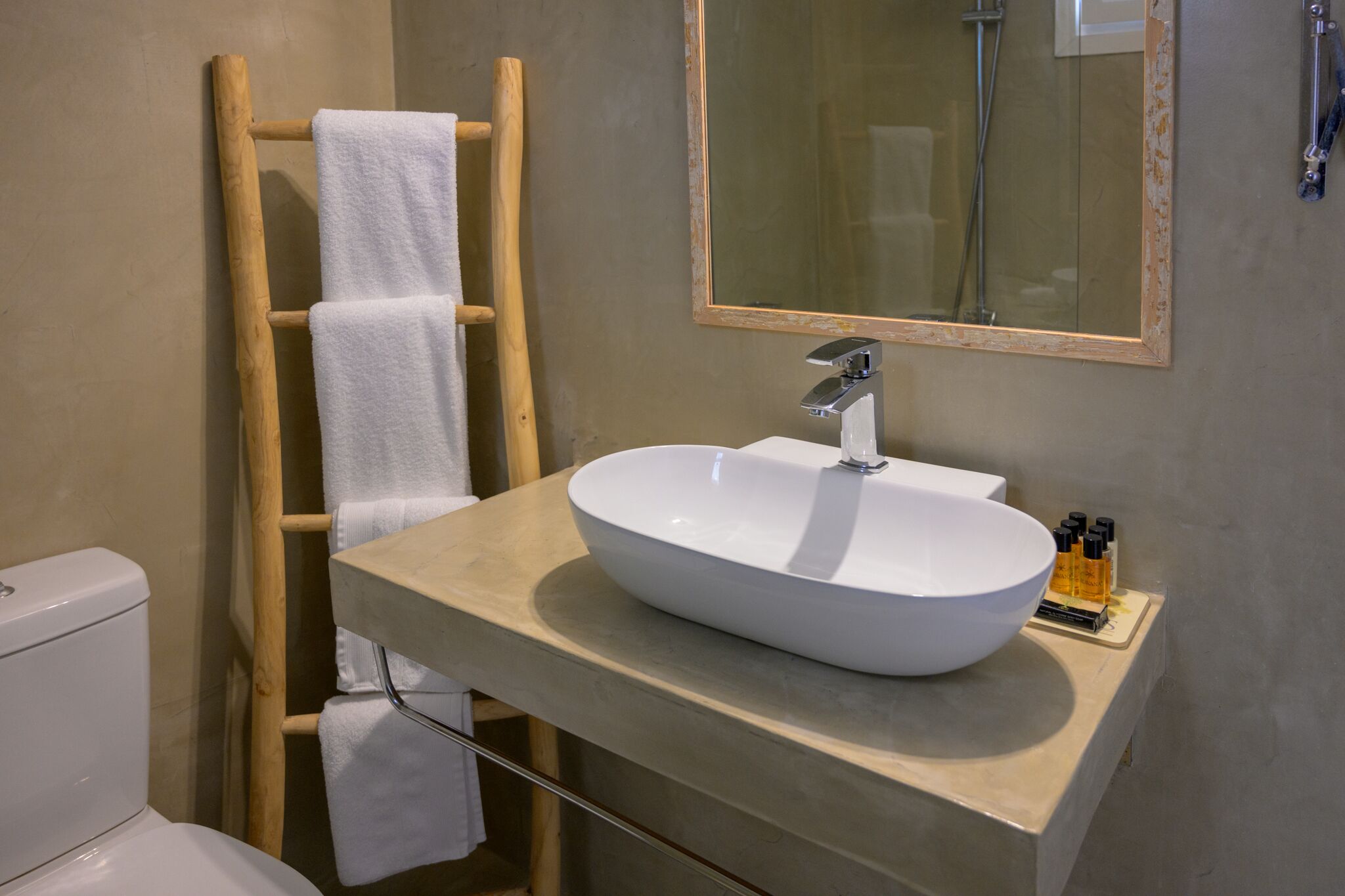 A bathroom with a wooden towel rack, a white sink, and a mirror.